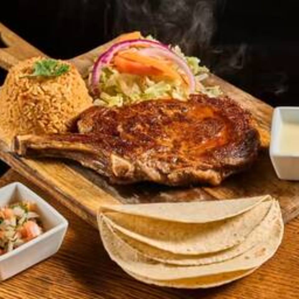Grilled fish fillet served with a vegetable-topped taco, tortillas, salsa, and lime on a wooden table.