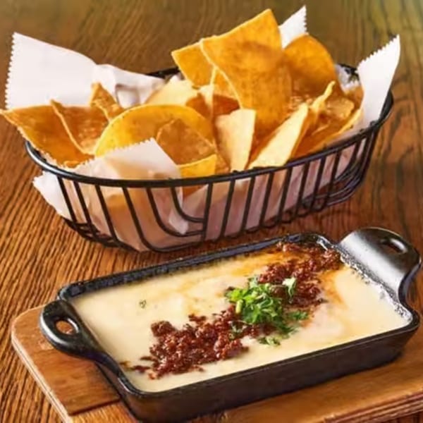 Basket of tortilla chips and a skillet of queso fundido with chorizo and cilantro.