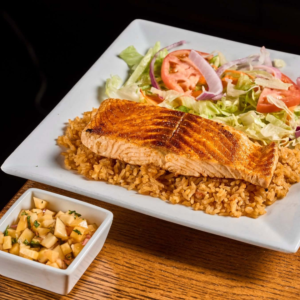 Grilled salmon fillet served over seasoned rice with a fresh lettuce, tomato, and onion salad.