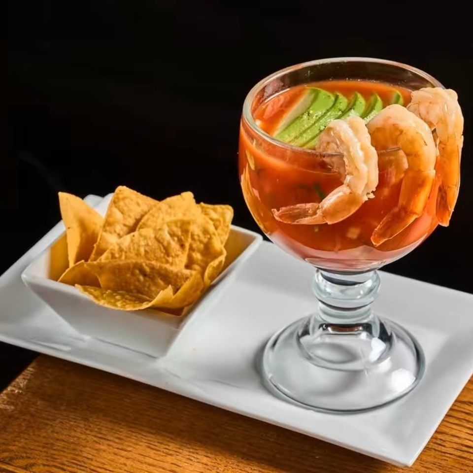 Shrimp cocktail with avocado slices and tortilla chips served on a white platter against a dark background.
