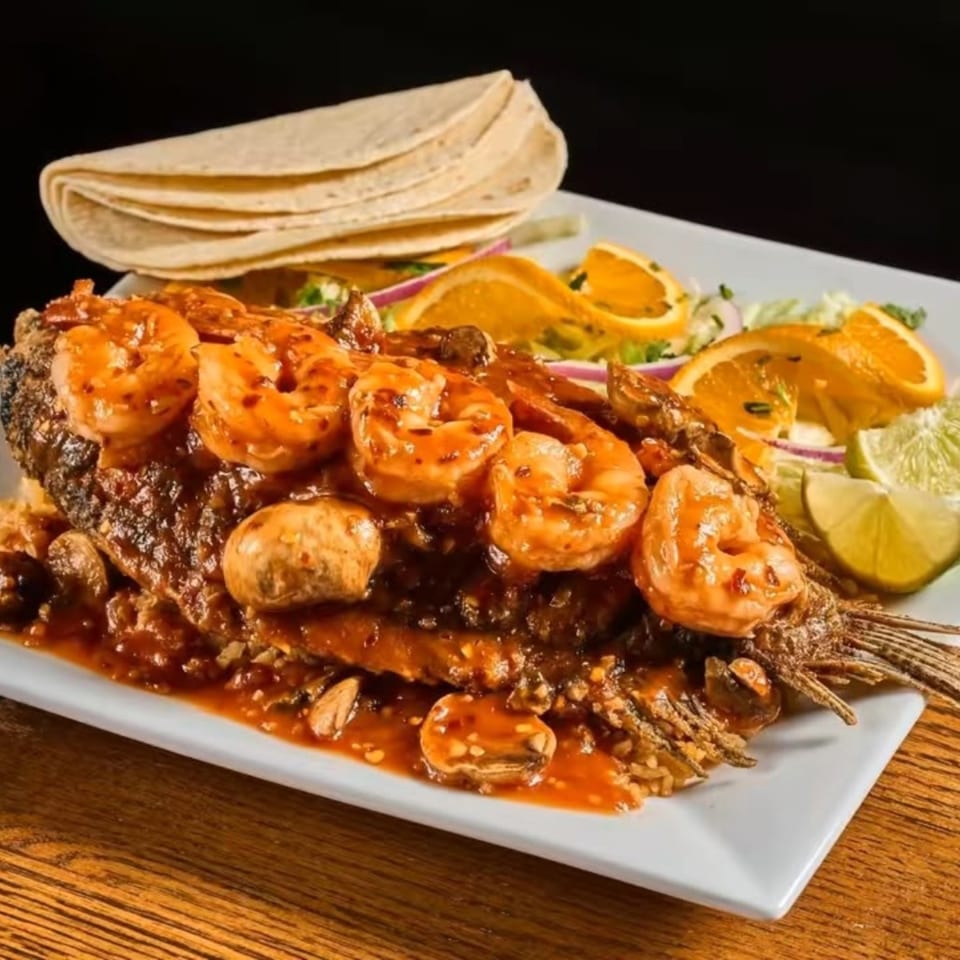 Grilled meat and shrimp platter with tortillas, salad, lime, and roasted vegetables on a white plate.