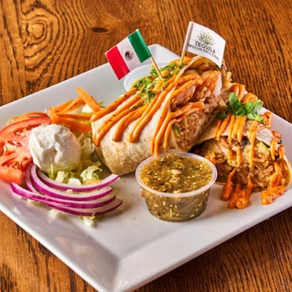 Mexican platter with tacos, fries, salad, grilled meat, dipping sauce, and Mexican and Tequila flags on a wooden table.