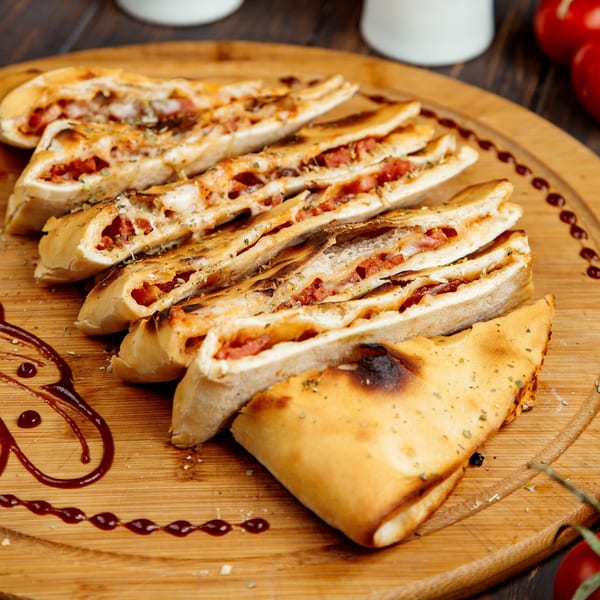 Sliced Tequila Mexican Grill & Bar calzone with melted cheese and red filling on a wooden board.