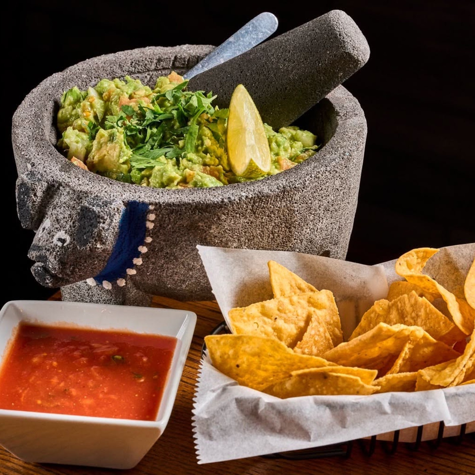 Fresh guacamole with lime in a stone molcajete, served alongside tortilla chips and red salsa.