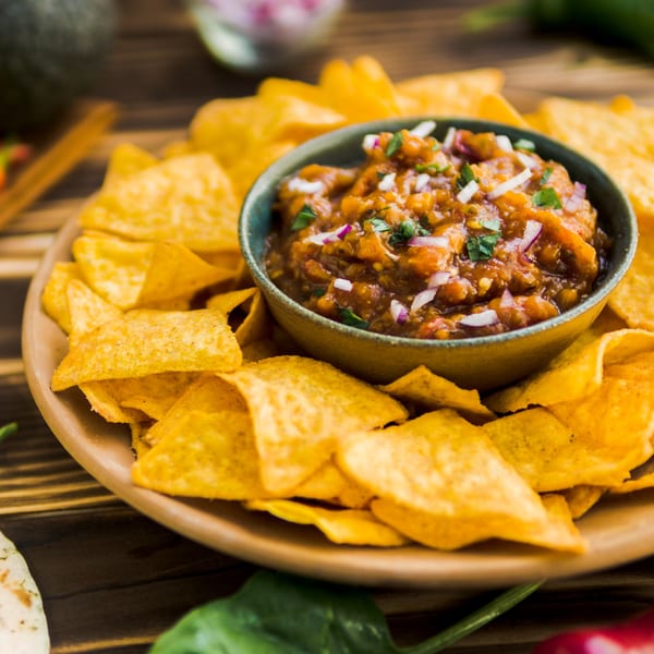 A bowl of Tequila Mexican Grill & Bar's salsa, topped with red onion and cilantro, surrounded by tortilla chips.