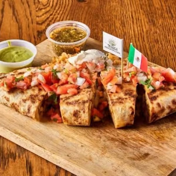 Grilled burrito cut into sections, topped with pico de gallo, served with sauces and Mexican flags.
